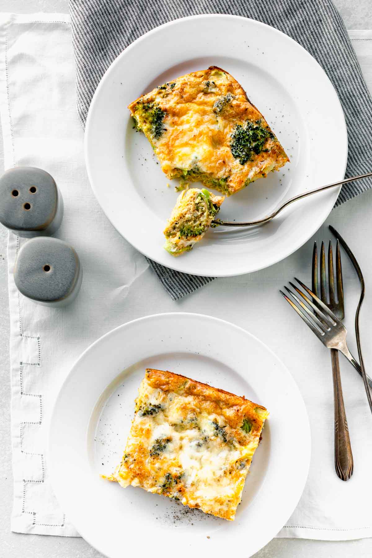 broccoli egg bake slices on white plates with gray salt and pepper shakers
