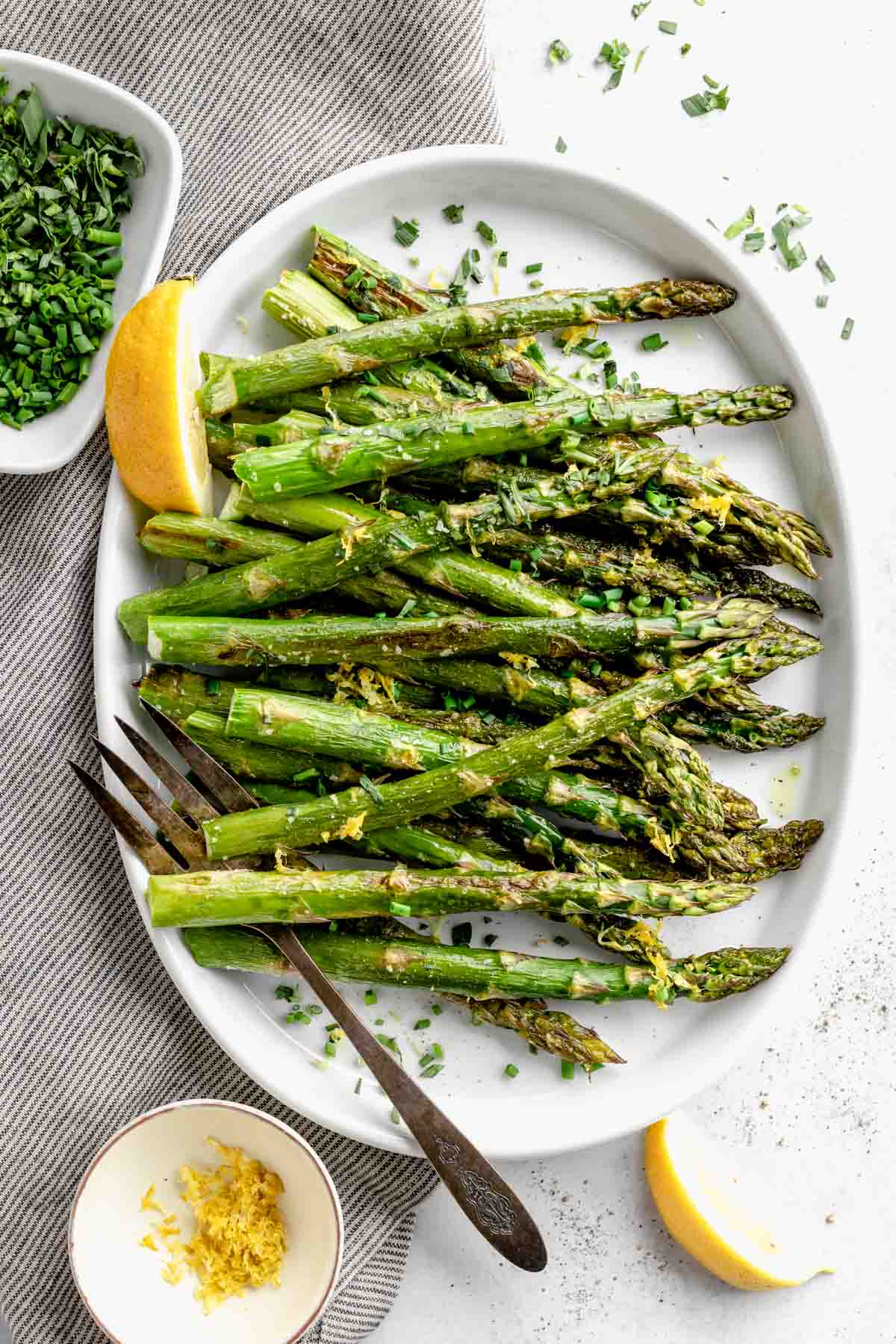 a platter of roasted asparagus with lemon zest, herbs and lemon wedges
