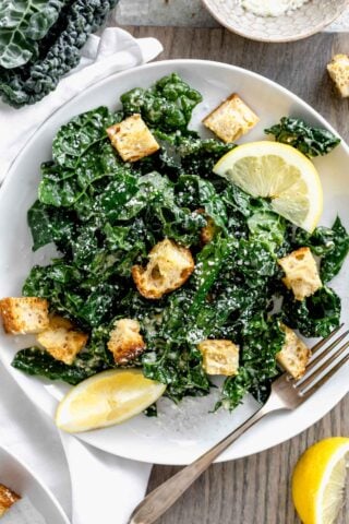 close up of a plate of caesar with lemon wedges