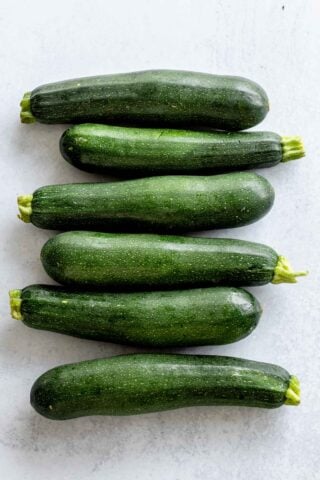 six medium, deep green zucchinis on a light colored table