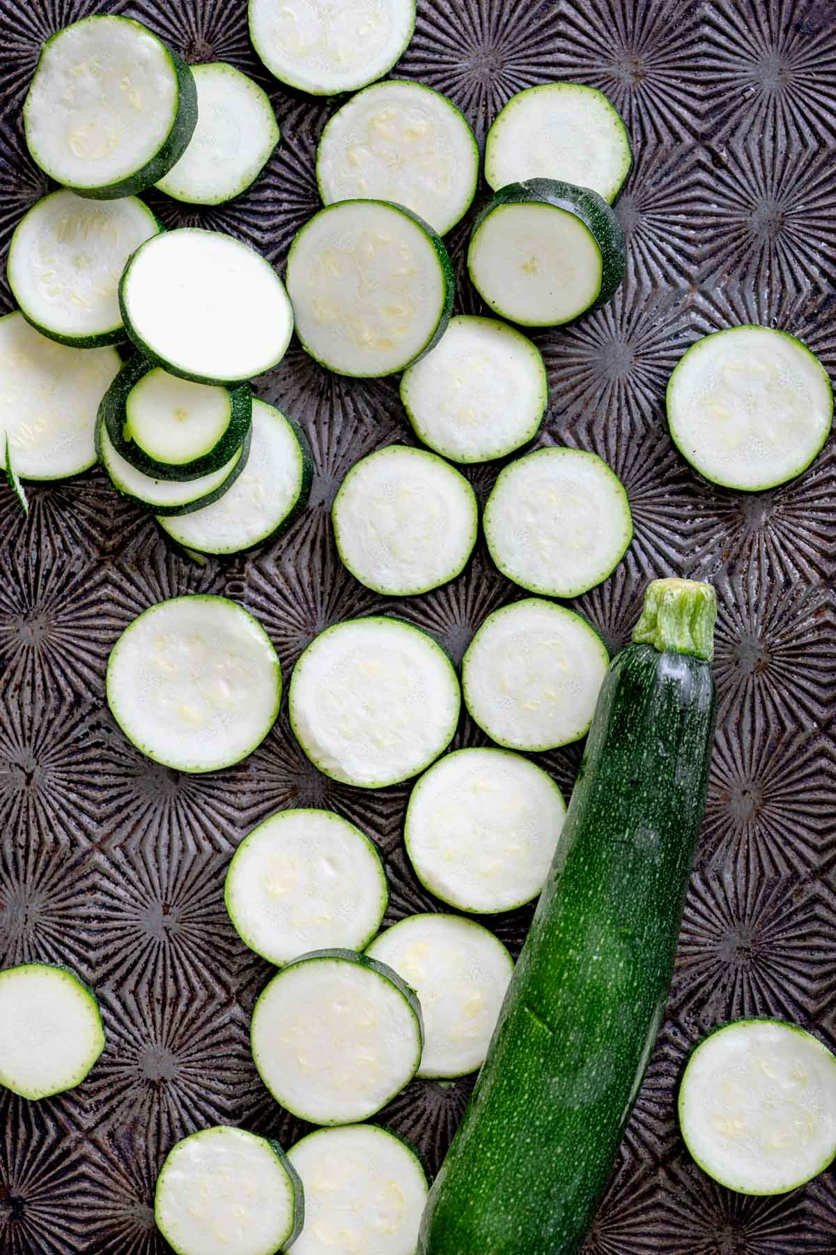 Zucchini coins and one whole green zucchini on a dark table.