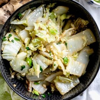 sauteed Napa cabbage in a black bowl with scallions and sesame seeds