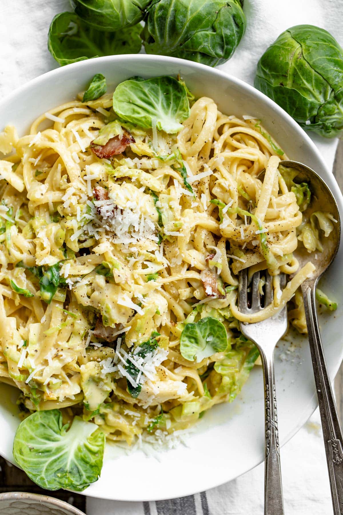 the brussels sprouts carbonara in a white bowl with fork and spoon