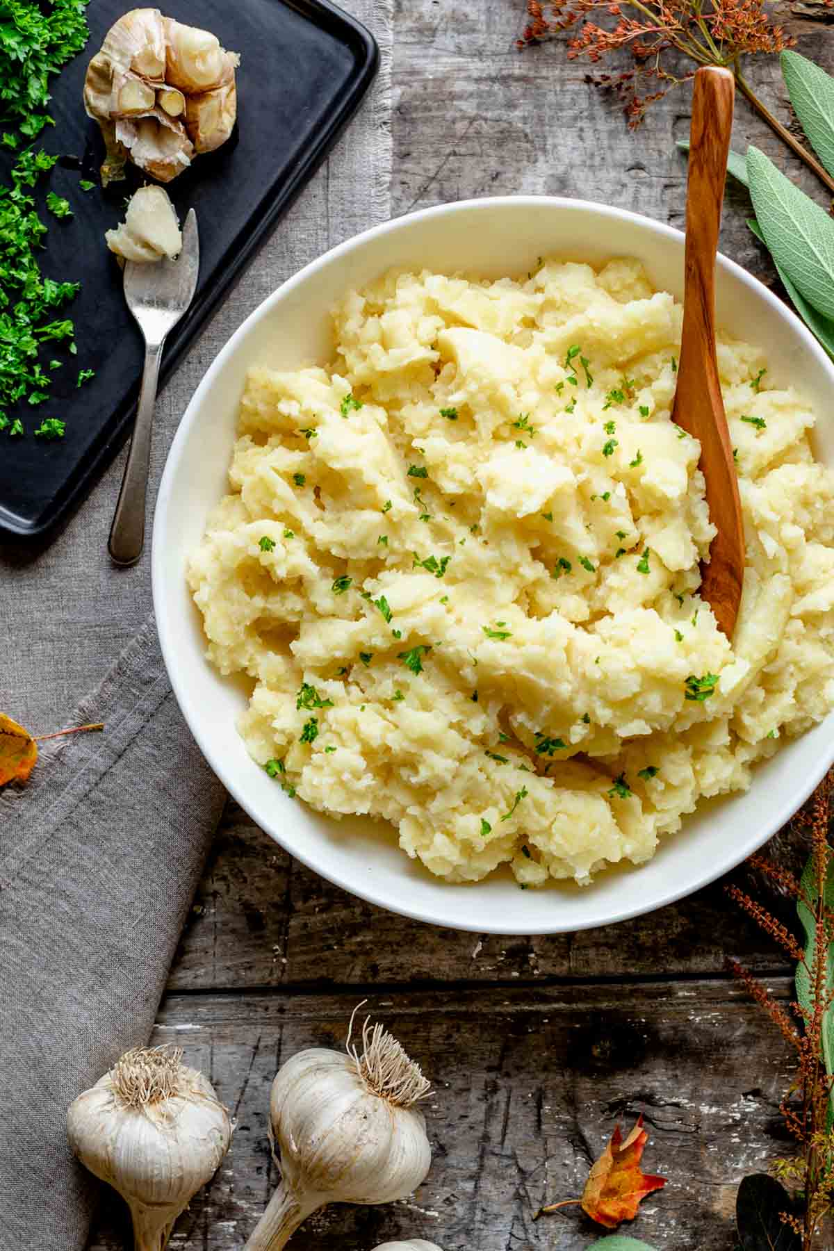 the potatoes in a white bowl and a head of roasted garlic