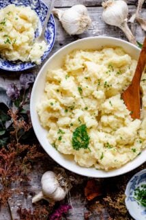 Close up overhead of the bowl of mashed potatoes, a serving in a blue bowl and foliage on the table.