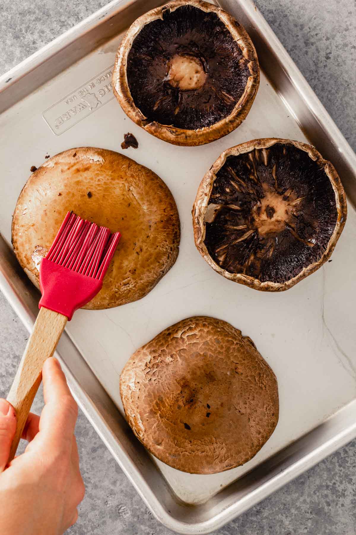 portobello mushrooms on a baking sheet getting brushed with oil