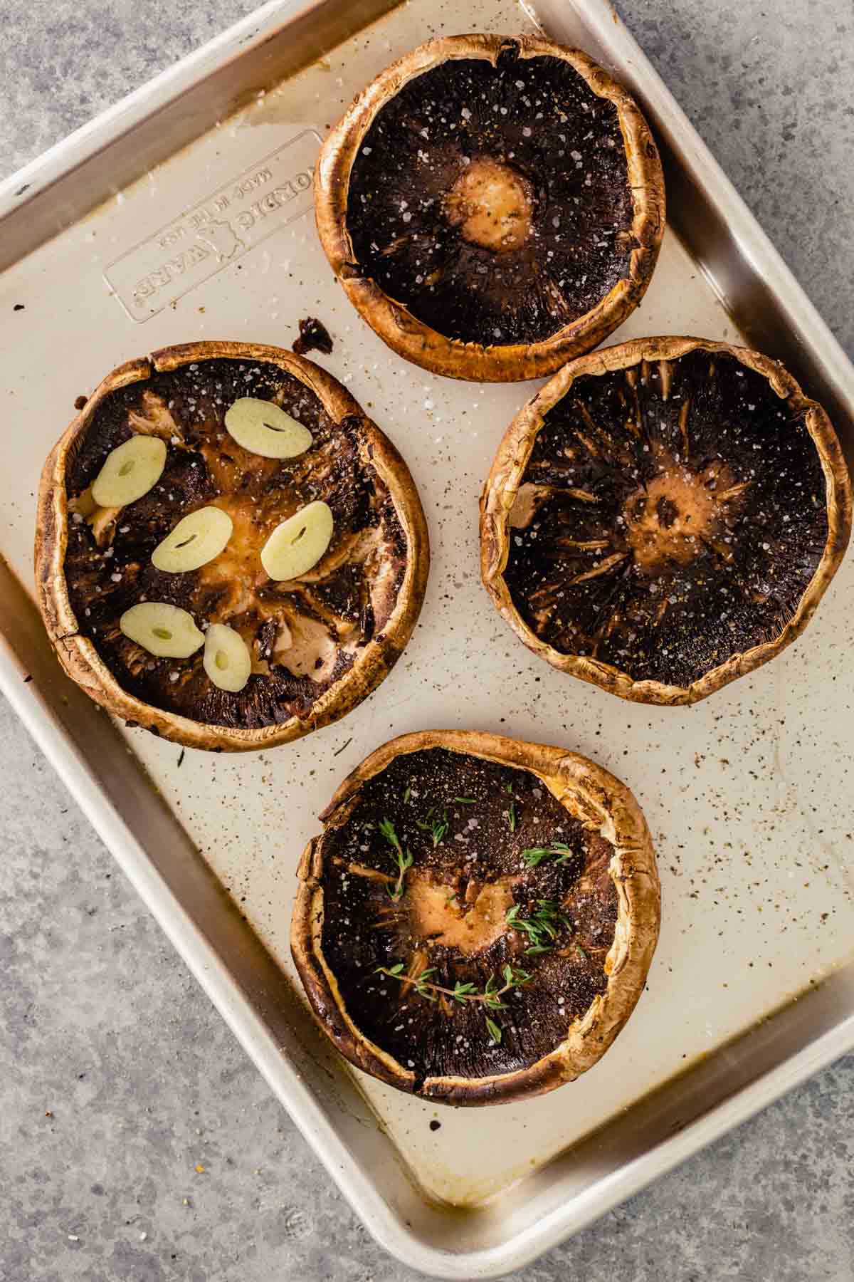 portobello mushrooms on baking sheet, a few with herbs or garlic sprinkled in them