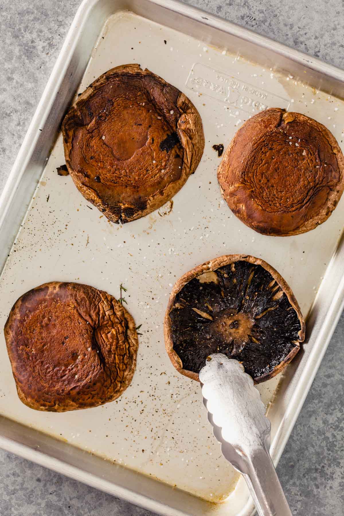 portobello mushrooms on a baking sheet getting flipped with tongs