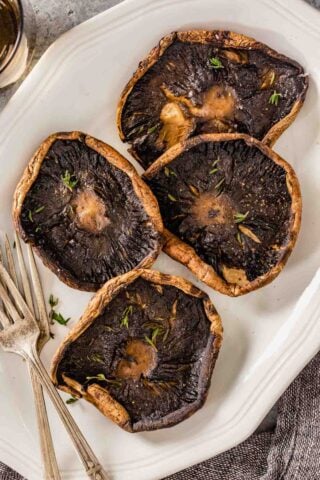 roasted portobello mushrooms on a white serving plate topped with fresh thyme leaves