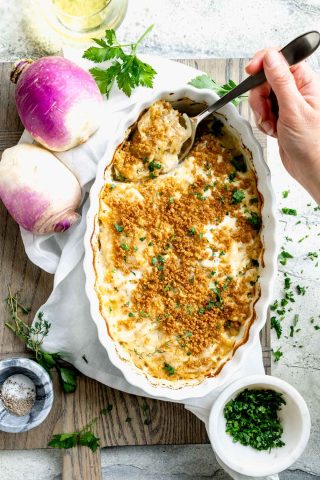 turnip casserole in scalloped white baking dish with serving spoon and ingredients