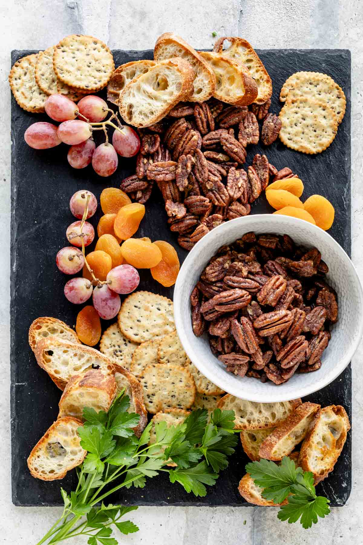 the nuts on a slate board with dried fruit, grapes and crostini