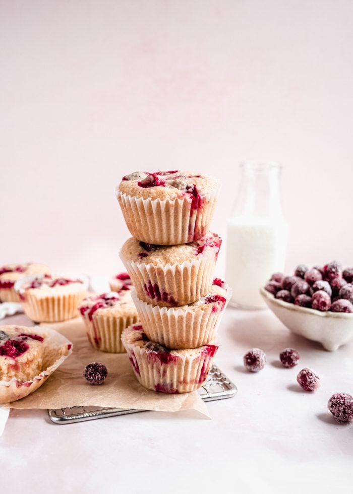 Cranberry orange muffins stacked atop each other on cooling rack with sugared cranberries on counter
