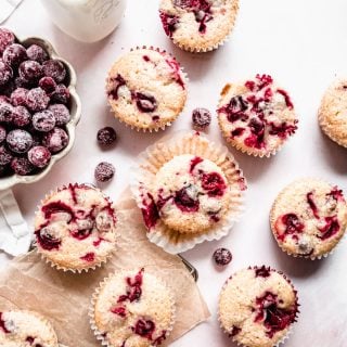 Cranberry orange muffins on parchment paper on counter, sugared cranberries in a bowl