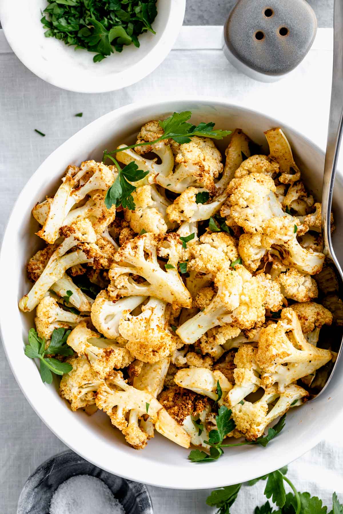 overhead photo of air fried cauliflower in circular white dish with serving spoon