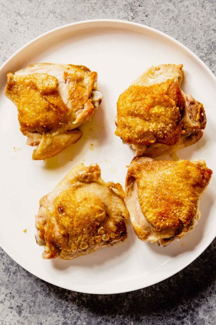crispy browned chicken thighs on a white plate