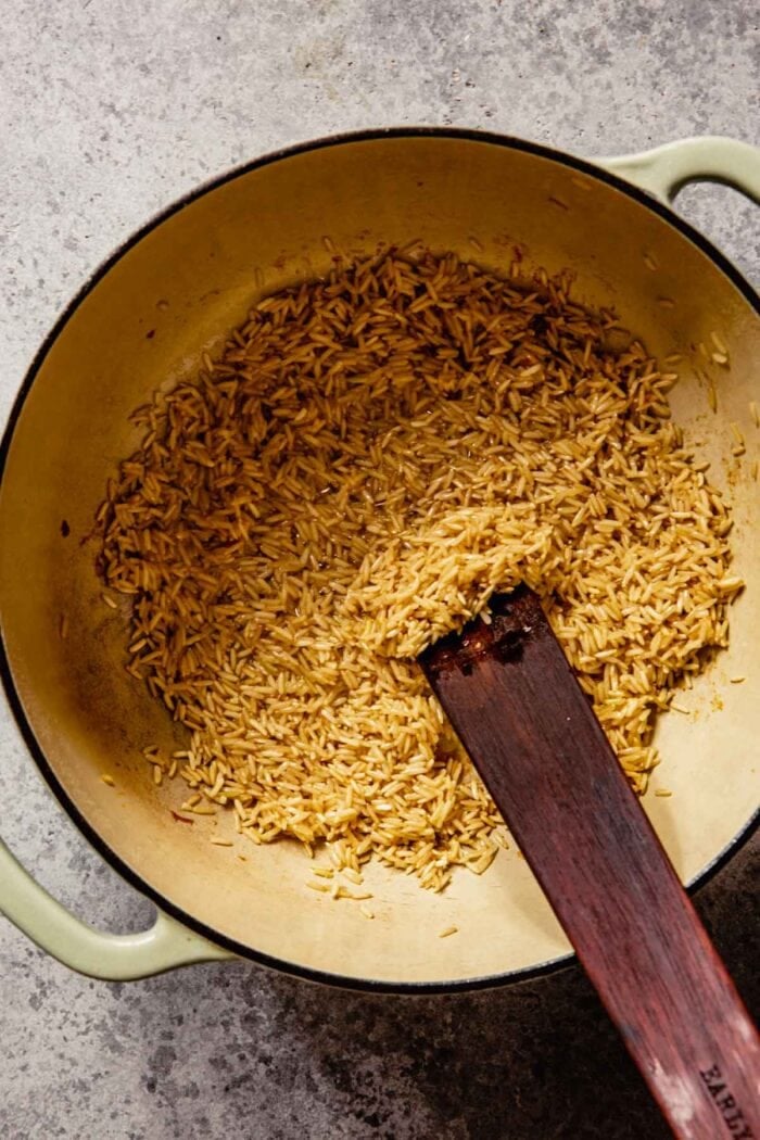 rice cooking in drippings in a large pot with a wooden cooking utensil