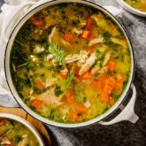 chicken and rice soup with vegetables in a pot on a table with two bowls of soup set around it