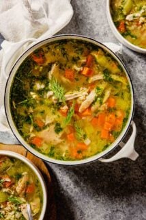 chicken and rice soup with vegetables in a pot on a table with two bowls of soup set around it