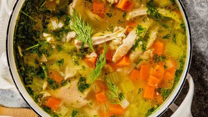 chicken and rice soup with vegetables in a pot on a table with two bowls of soup set around it