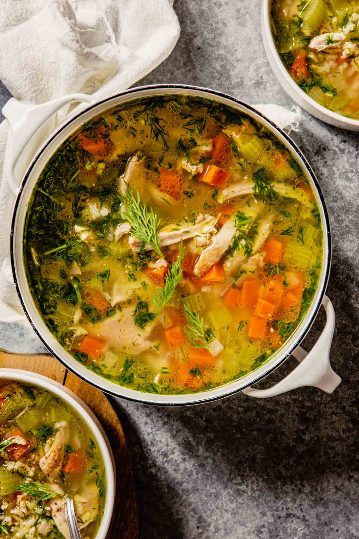 chicken and rice soup with vegetables in a pot on a table with two bowls of soup set around it