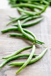 a still life of fresh green beans on a wooden cutting board