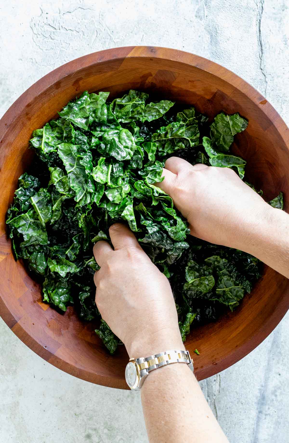 the kale in a wooden salad bowl with two hands massaging it