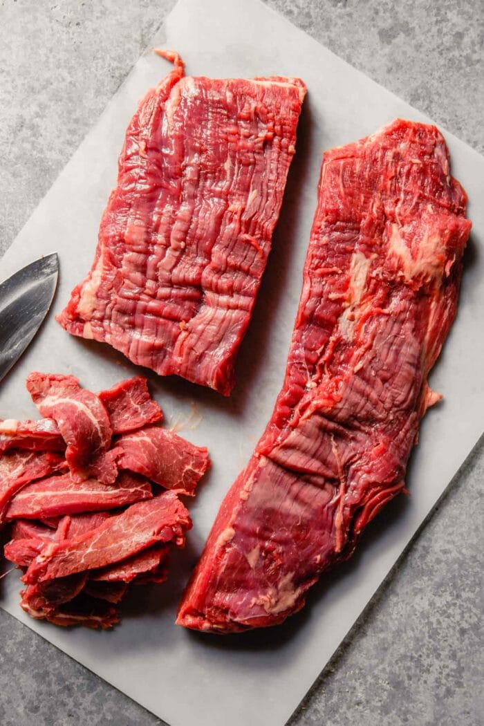 flank steak cut in half lengthwise on a plastic cutting board and getting thinly sliced