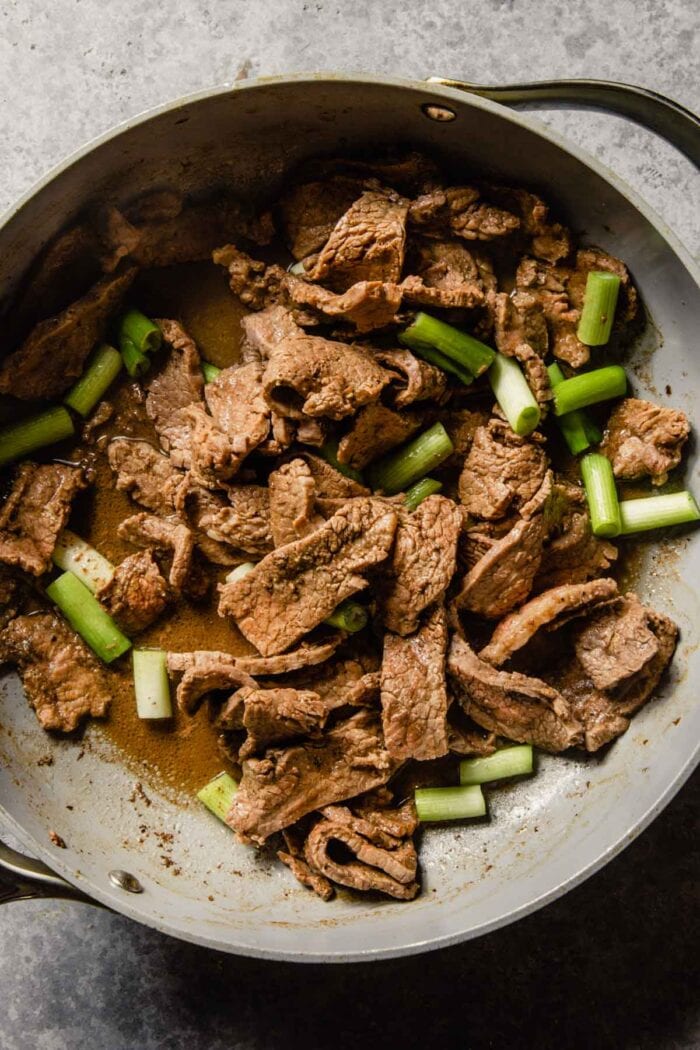 thinly sliced beef in a skillet with scallions