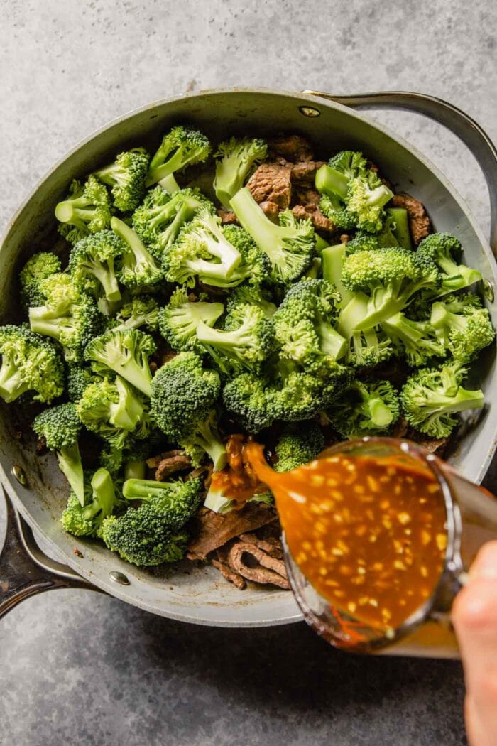 sauce being poured into skillet with broccoli