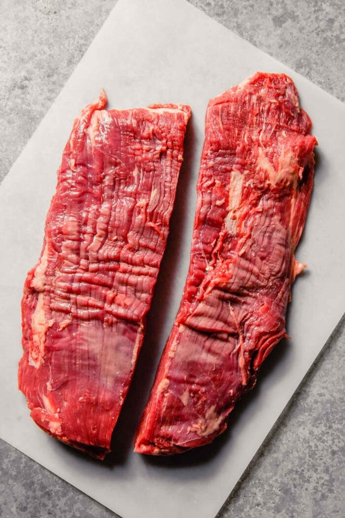 flank steak cut in half lengthwise on a plastic cutting board