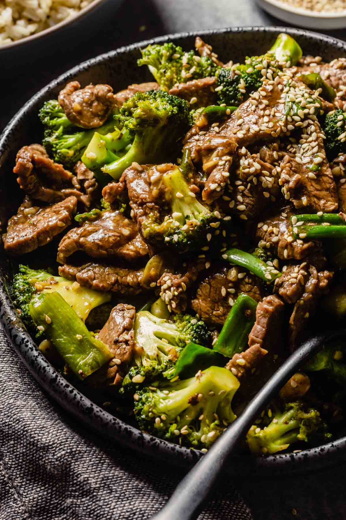 thinly sliced cooked steak and broccoli coated in a sauce and piled into a black bowl