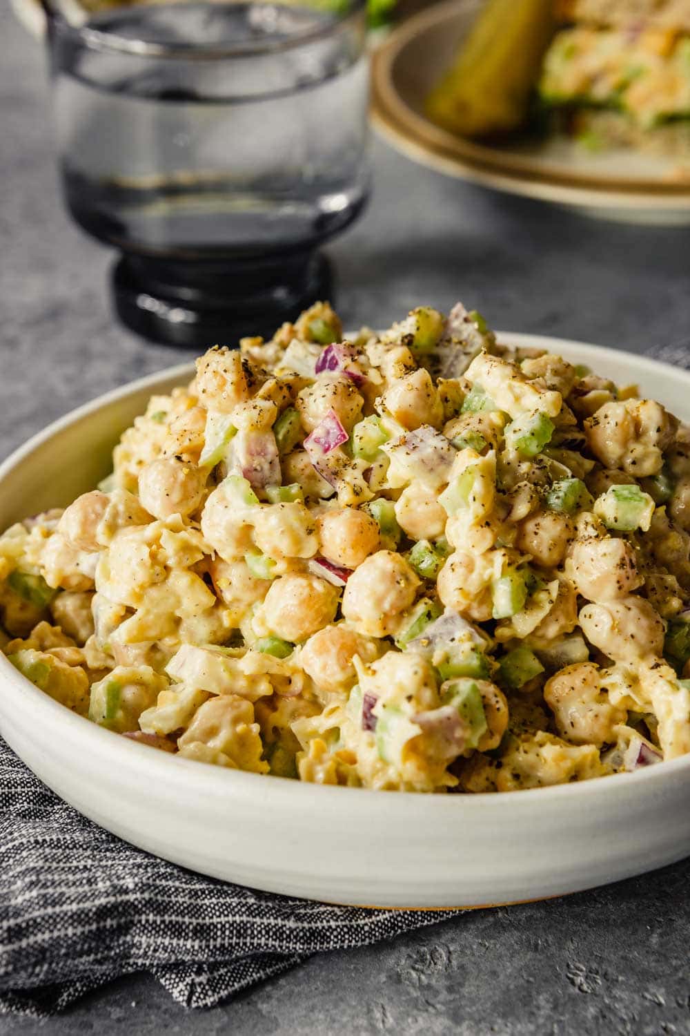 chickpea tuna salad in a shallow white bowl with a plate and glass in the background