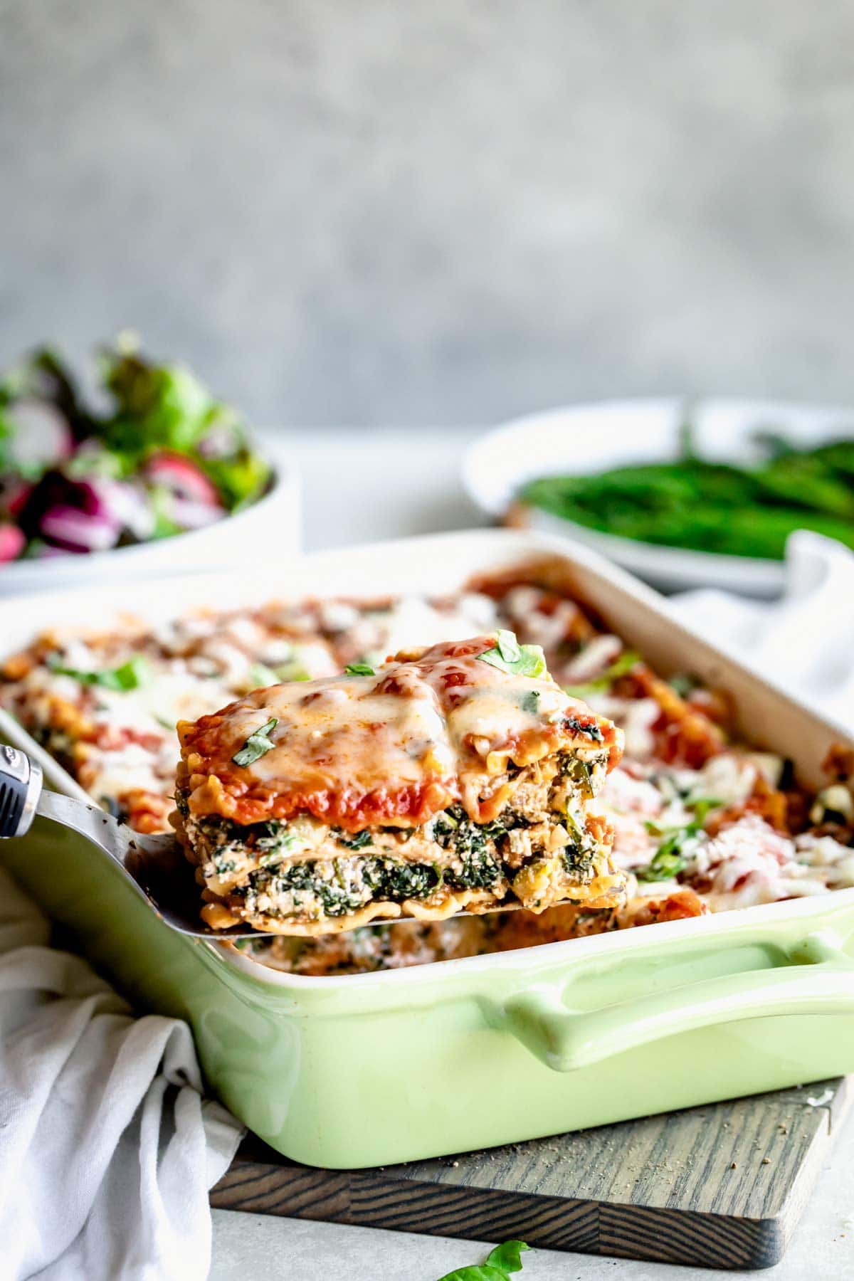 Baked vegetarian lasagna in baking dish with slice sitting on spatula.