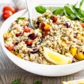 Side view of Mediterranean barley salad in circular white bowl with a serving spoon in the dish.