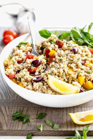 Side view of Mediterranean barley salad in circular white bowl with a serving spoon in the dish.