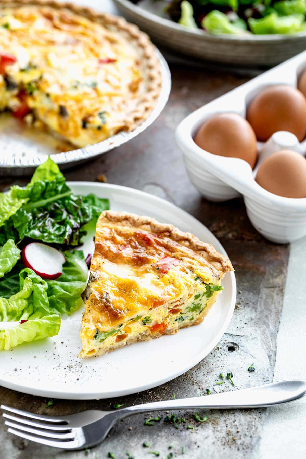 slice of vegetable quiche on circular white plate with side salad.