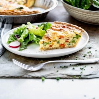 side view of a slice of quiche on white plate with a side salad.