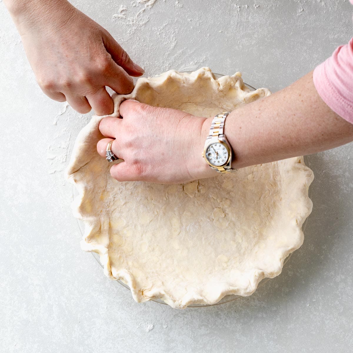 overhead shot of homemade pie crust being pinched in pie plate.