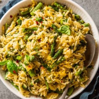 cooked orzo and asparagus in a white bowl topped with fresh herbs