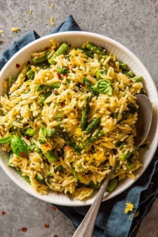 cooked orzo and asparagus in a white bowl topped with fresh herbs