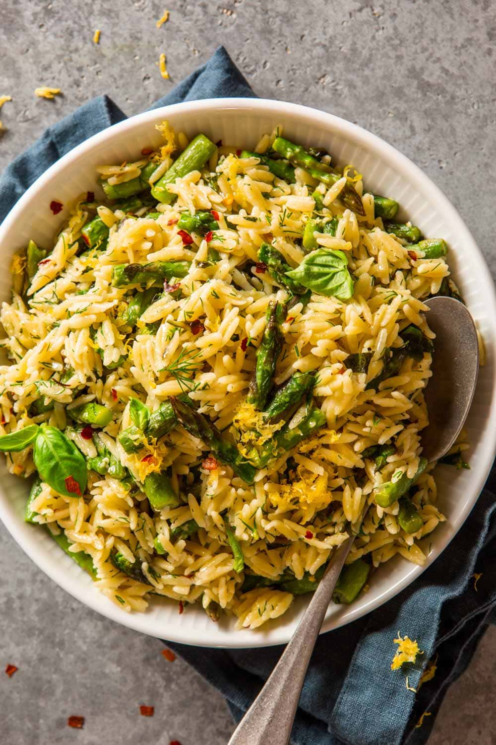 cooked orzo and asparagus in a white bowl topped with fresh herbs