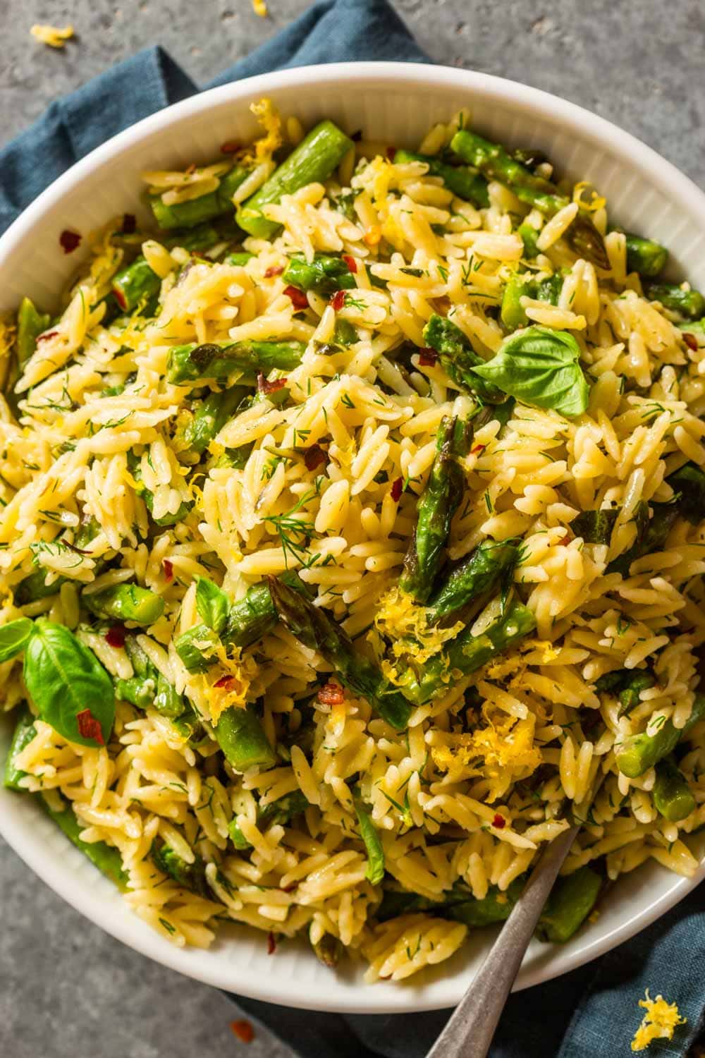 cooked orzo and asparagus in a white bowl topped with fresh herbs