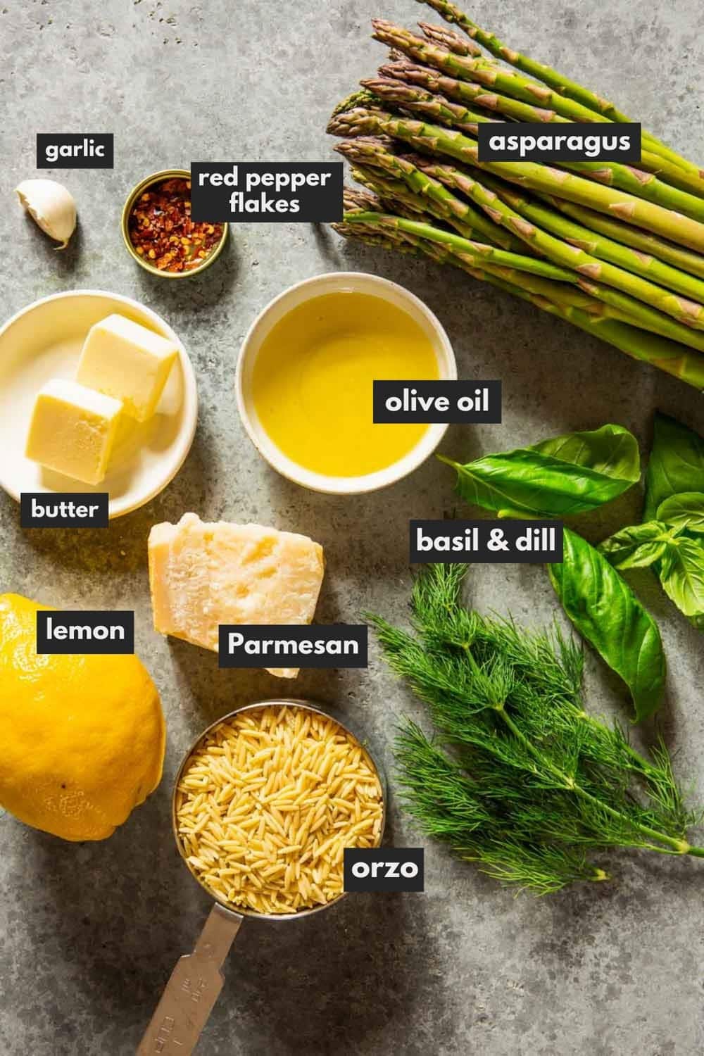 lemon, oil, garlic clove, red pepper, asparagus, herbs, dry orzo paste, parmesan arranged on a counter