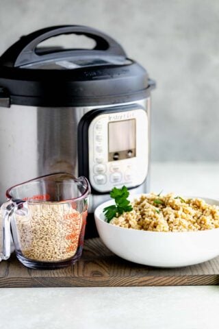 instant pot with a bowl of cooked barley and a measuring cup with uncooked barley