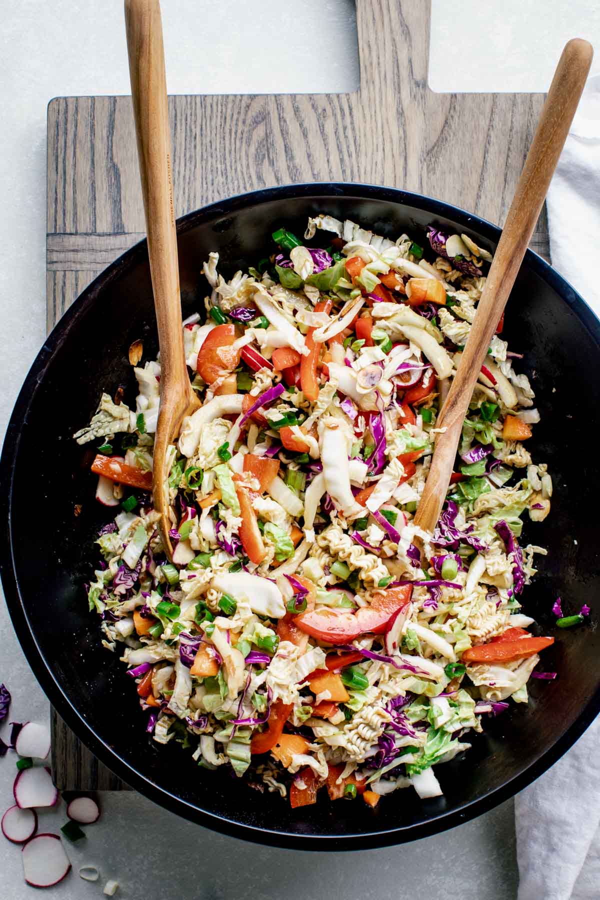 Top view of Napa Cabbage Ramen Noodle Salad in a black bowl with wooden serving spoons in it.