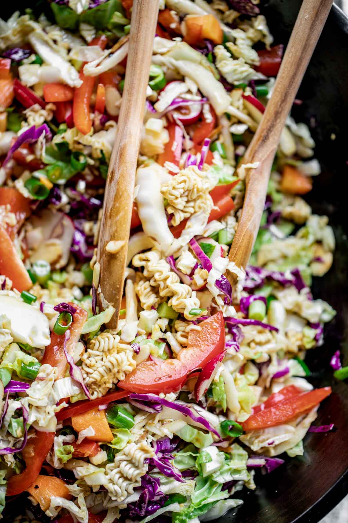 Close up of napa cabbage salad in a black bowl with wooden salad spoons in it.