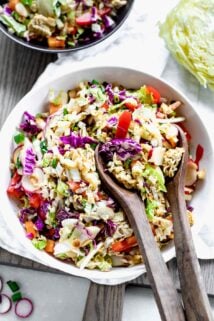 Napa Cabbage Ramen Noodle Salad in a white bowl with wooden salad spoons in it on a table.