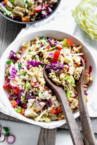 Napa Cabbage Ramen Noodle Salad in a white bowl with wooden salad spoons in it on a table.