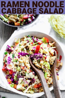 Napa Cabbage Ramen Noodle Salad in a black bowl with wooden serving spoons in it, with a text box on the top with the title "Napa Cabbage Ramen Noodle Salad" on it.