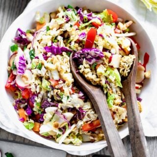 Napa Cabbage Ramen Noodle Salad in a white bowl with wooden salad spoons sitting in it.